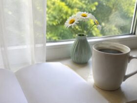 Чашка кави, розгорнутий блокнот і ромашки на підвіконні